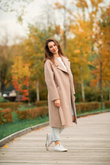 A Caucasian girl in a pink coat and blue jeans with holes dances in an autumn park