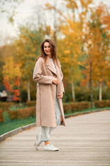 A Caucasian girl in a pink coat and blue jeans with holes dances in an autumn park