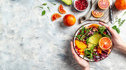 Girl holding vegan, detox Buddha bowl with avocado, persimmon, blood orange, nuts, spinach, arugula and pomegranate, balanced food. space for text. top view
