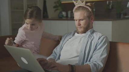 Little daughter playing and making up man as princess, sitting on the sofa at home. Father's day.