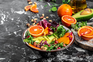 Buddha bowl dish with avocado, persimmon, blood orange, nuts, spinach, arugula and pomegranate. Healthy balanced eating. Top view
