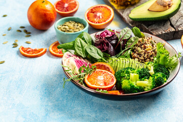 Healthy vegetarian buddha bowl salad with vegetables, avocado, blood orange, broccoli, watermelon radish, spinach, quinoa, pumpkin seeds on a blue background.