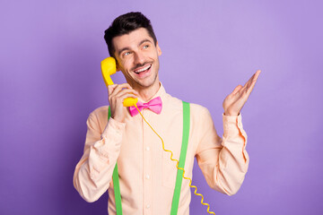 Photo of pretty cheerful man dressed yellow shirt talking vintage yellow phone looking empty space isolated purple color background