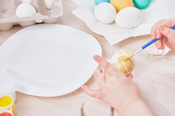child paints egg for Easter on a wooden table,
