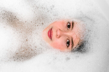 Girl face in  bathtub in water with foam.