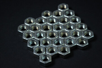 Nut bolts on a black background. threaded fastener. The nut bolts are neatly stacked in several rows, the rows fit snugly together