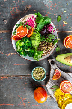 Vegan Buddha bowl with vegetables, avocado, blood orange, broccoli, watermelon radish, spinach, quinoa, pumpkin seeds. Balanced food. Delicious detox diet. Top view. vertical image
