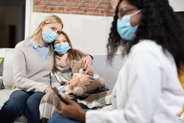 Beautiul skilled black-skinned woman in medical gown visiting sick teen girl which is ill at home...