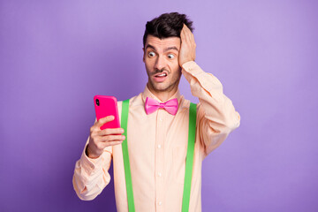 Photo of shocked astonished brunette man hold hand head look read fake news phone isolated on...