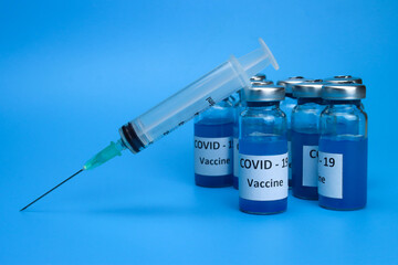 Ampoules with coronavirus vaccine and a syringe on a blue background. The concept of the fight against ncov COVID-19 pandemic