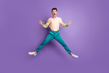 Full size photo of funky funny man jump up air pull green suspenders pink bowtie isolated on purple color background