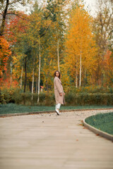 Fototapeta premium A girl with a Euro-Asian appearance in a pink coat and blue jeans with holes walks in an autumn park