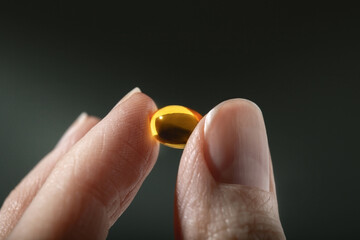 Female hand holding a small yellow capsule of nutritional supplement. Food supplement, vitamin D, omega, vitamin C, multivitamins. Soft focus