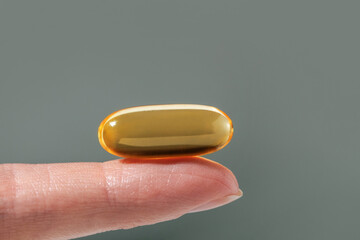 Female hand holding a big yellow capsule of nutritional supplement . Food supplement, vitamin D, omega, vitamin C, multivitamins