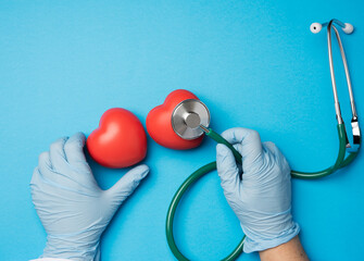two hands hold medical stethoscope and red rubber heart on a blue background,