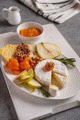 Brie cheese with nuts, pear slices and dried apricots. Camembert cheese. Brie cheese or Camembert cheese  on a wooden board. Tasty cheese starter.