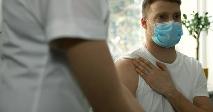 doctor injecting vaccine in shoulder of young man with face mask in clinic. immunization and vaccination