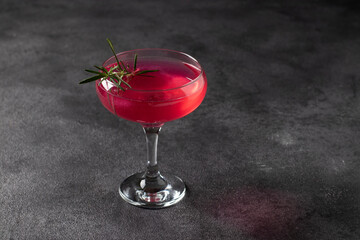 Sparkling rose wine with a shimmering edible sheen, garnished with rosemary on a dark background
