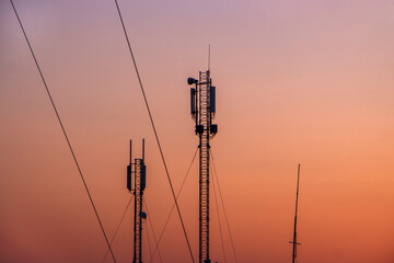 Tower with a mobile signal transmitter on the background of an orange cloudless sky in the morning.