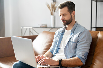 Clever freelancer using laptop for remote work from home. A handsome bearded guy websurfing, sends...