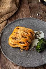 Puff pastry with meat and cheese on top served with mashed spinach and white sauce. Close-up of the dish on a grey plate isolated on wooden background with a sacking by side. Vertical orientation.