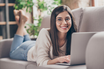 Naklejka premium Photo of cheerful positive girl use laptop lie sofa in living room stay home good mood inside house indoors home