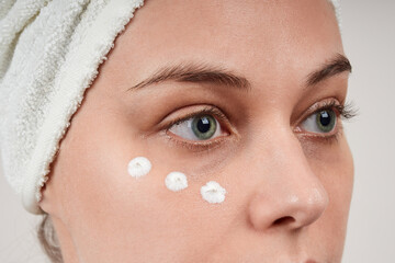 Close-up of a beautiful young woman applies cream under the eyes, anti-wrinkle face skin care. Isolate on gray background