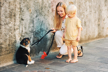 Outdoor portrait of happy young mother presenting puppy to toddler boy