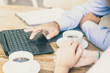 Cropped shot of manager and customer meeting over cup of coffee, sitting at table and using laptop, discussing content. Closeup of hands and table. Consulting or cooperation concept