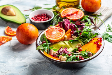 Buddha bowl dish with avocado, persimmon, blood orange, nuts, spinach, arugula and pomegranate. Healthy balanced eating. Top view