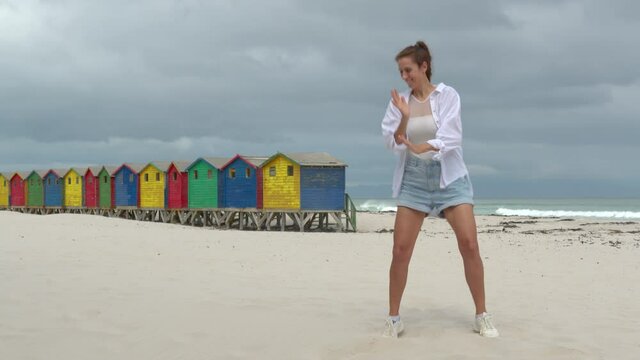 A girl dancing on the white sands of South Africa near the colorful wood Muizenberg Beach Houses.