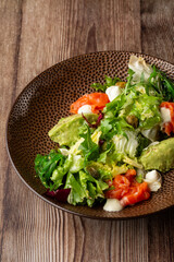 A salad with smoked salmon, mashed avocado and lettuce dressed with cream cheese. Close-up of the dish in a brown bowl isolated on wooden background. Vertical orientation.
