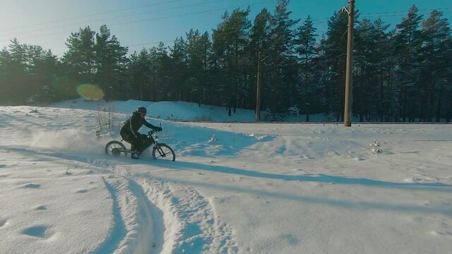 Cyclist in Black Clothes, Helmet and Snow Glasses Riding on Electric Bike in the Snow in Winter Forest. E-Bike Riding and Drifting at Cold Sunny Day - Super Slow Motion