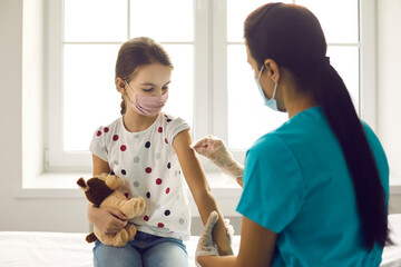 Vaccination concept. Little kid in medical face mask getting Covid-19 or flu vaccine at clinic....
