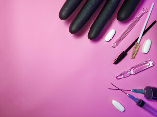 Medical cosmetology. Gloves, syringes, ampoule pills and brushes for eyelashes and eyebrows on a pink background side view
