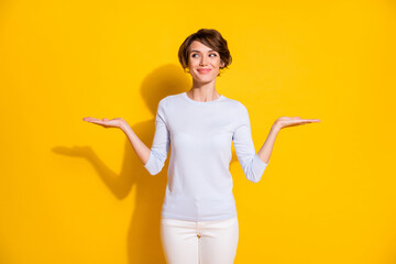 Photo of charming lady raise two palms look empty space wear white shirt trousers isolated yellow...