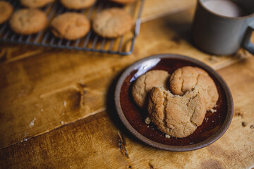 a delicious looking batch of snickerdoodle cookies and some warm milk in a rustic looking cup. the cookies are freshly baked and have   Cinnamon and sugar on them. the cow milk is fresh and warm. 