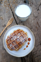 Top view Waffles  with caramel  syrup in a white plate and fresh milk in a glass placed on the table.