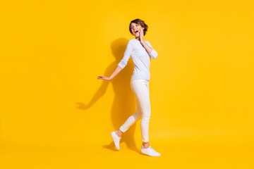 Fototapeta na wymiar Full length photo of charming sweet young lady dressed white shirt walking looking back empty space isolated yellow color background