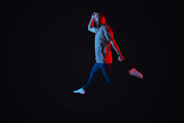 Photo of bearded man jumping over black background with neon blue and red lights.