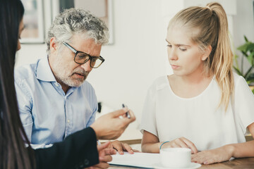 Obraz premium Focused mature man reading document, his female colleague giving pen to him for signing. Medium shot. Expertise or paperwork concept