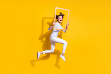 Fototapeta na wymiar Full length photo of funny sweet young lady dressed white shirt jumping holding photo frame isolated yellow color background