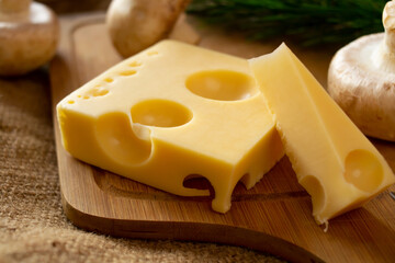 a piece of maasdam cheese, delicious cheese and mushrooms on a cutting board against a background of burlap