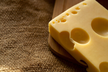 a piece of maasdam cheese, delicious cheese and mushrooms on a cutting board against a background of burlap