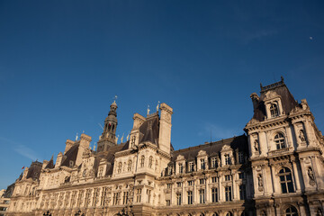 Fototapeta na wymiar Paris, France. Beautiful Parisian city hall (hotel de ville) in sunset golden lights and moon in dark blue sky and passing plane trace. Travel background. Europe capitals tourism concept.
