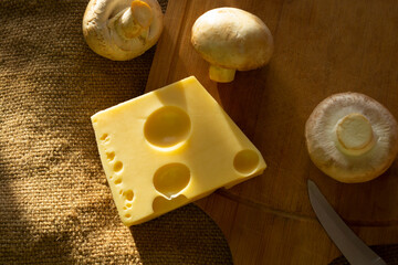 a piece of maasdam cheese, delicious cheese and mushrooms on a cutting board against a background of burlap
