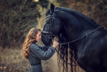Obraz premium Beautiful girl staying near black Frisian horse in spring in the forest