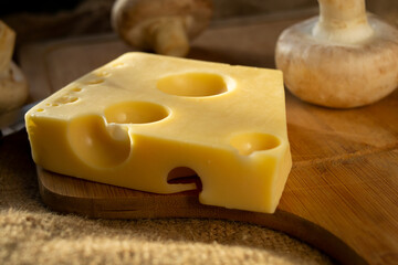 a piece of maasdam cheese, delicious cheese and mushrooms on a cutting board against a background of burlap