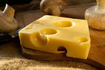 a piece of maasdam cheese, delicious cheese and mushrooms on a cutting board against a background of burlap