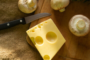 a piece of maasdam cheese, delicious cheese and mushrooms on a cutting board against a background of burlap